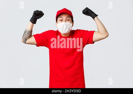 Fröhlicher asiatischer Entführer in medizinischer Maske und Handschuhen, trägt Trägeruniform, singt mit der Faust, sagt ja oder hufig glücklich, Stockfoto