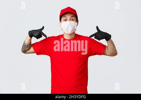 Glücklicher asiatischer Lieferer in roter Uniform, Mütze und T-Shirt, mit Schutzhandschuhen und Maske während des Zuges 19 Quarantäne, Pandemie Stockfoto