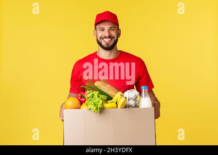 Online-Lieferung, Shopping und Food Order Konzept. Netter Lieferer, Kurier in roter Uniform, bringen Sie Lebensmittelbestellung im Karton mit Stockfoto
