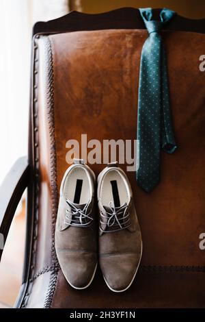 Herrenschuhe und Krawatte auf einem braunen Lederstuhl. Stockfoto