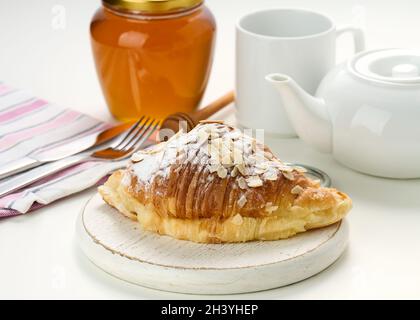 Gebackene knusprige Croissants werden mit Zuckerpulver und Mandelflocken auf einem Holzbrett, weißem Keramikgebräu und einer Tasse auf einem Weißbrot bestreut Stockfoto