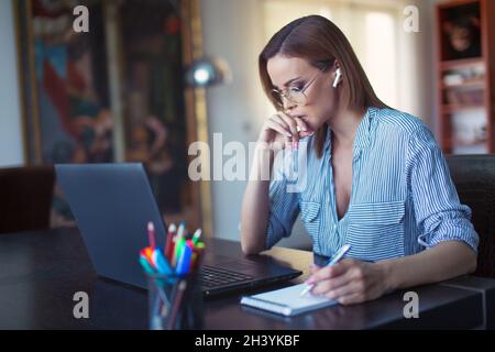 Junge Nerd kaukasische Geschäftsfrau macht Notizen auf Notebook am Laptop Stockfoto