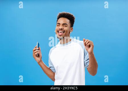 Porträt eines fröhlichen und sorglosen, gutaussehenden, urbanen afroamerikanischen Mannes in einem lässigen T-Shirt, der mit seinen Lieblingssongs tanzt Stockfoto