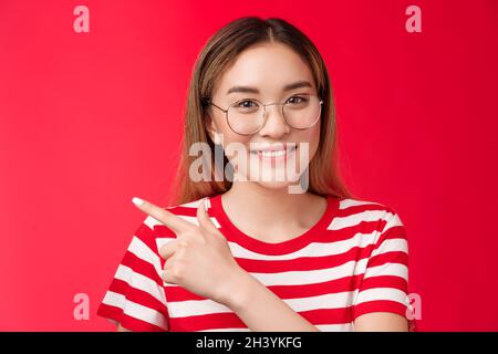 Gute Gelegenheit hinter der Ecke. Nettes asiatisches Mädchen trägt Brille gestreiftes Sommer-T-Shirt nach links zeigend, lächelnd toothy freundlich ex Stockfoto