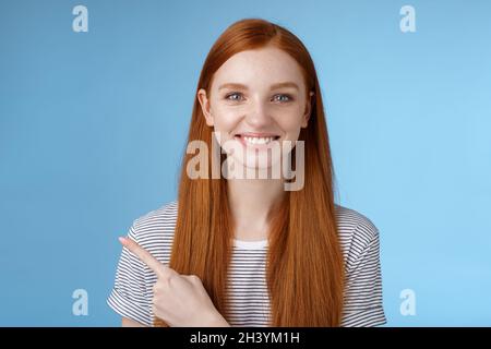 Angenehm charismatisch hilfreich freundlich aussehende weibliche rothaarige blaue Augen zeigen linken Zeigefinger helfen, Entscheidung treffen wählen Produk Stockfoto