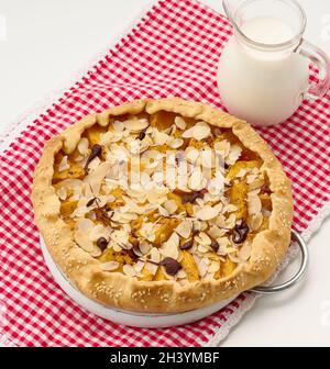 Gebackener runder Kuchen mit Apfelstücken, bestreut mit Mandelflocken auf einem weißen Tisch Stockfoto