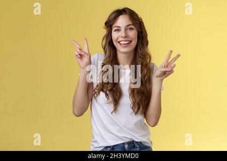 Freundlich friedlich charmant glücklich junge Mädchen lockig lange Haare zeigen Frieden Sieg Zeichen mit Spaß posiert ausgehenden lebhaften Blick kam Stockfoto