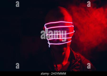 Porträt eines Mannes mit Neon-Leuchtröhren-Linien auf seinem Gesicht im Dunkeln. Konzept Cyberpunk und Virtual Reality. Stockfoto