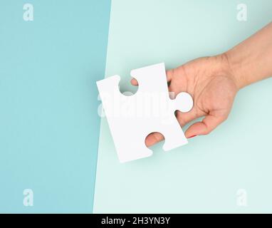 Weibliche Hand hält ein Fragment eines weißen großen Puzzles auf einem blauen Hintergrund Stockfoto