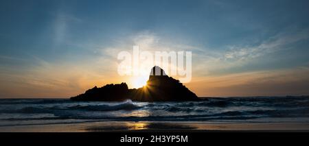 Karekare Strand bei Sonnenuntergang mit Sonnenstrahlen durch Panatahi Island, Waitakere, Auckland. Stockfoto