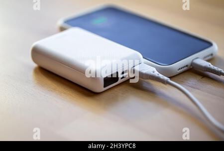 Ein Smartphone wird von einer kleinen weißen Powerbank geladen. Stockfoto
