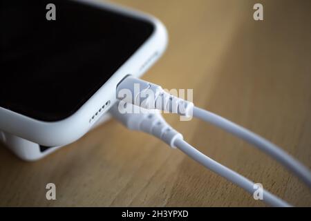 Ein Smartphone wird von einer kleinen weißen Powerbank geladen. Stockfoto