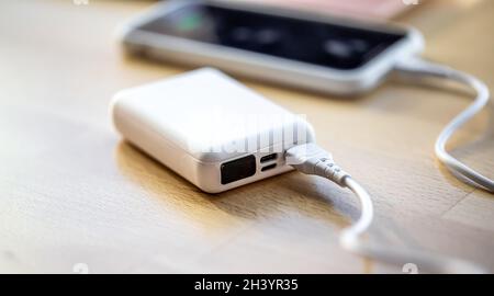 Ein Smartphone wird von einer kleinen weißen Powerbank geladen. Stockfoto