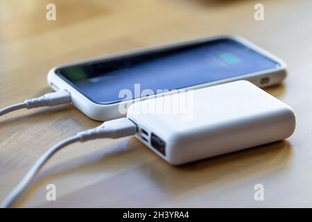 Ein Smartphone wird von einer kleinen weißen Powerbank geladen. Stockfoto