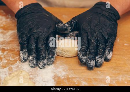 Koch Hände in schwarzen Handschuhen bereitet Teig aus nächster Nähe Stockfoto