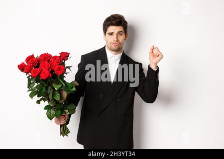 Bild von eleganten und frechen Mann in schwarzem Anzug, zuversichtlich und hält Strauß von roten Rosen, gehen auf ein romantisches Date, Stan Stockfoto