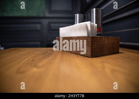 Holzkiste mit Gewürzen und Servietten auf einem Tisch in einem Café. Stockfoto