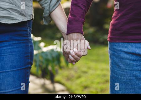 Mittelteil eines älteren kaukasischen Paares, das Hände beim Gehen im Garten hält Stockfoto