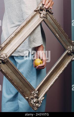 Junger Mann steht mit Bilderrahmen und Apfel im Studio. Stockfoto