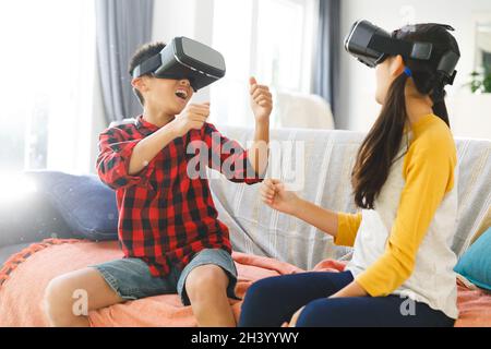 Lächelnder asiatischer Bruder und Schwester sitzen auf der Couch und benutzen vr-Headsets Stockfoto