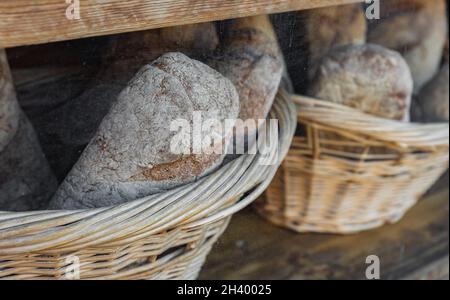 Backstube mit Vitresen voll mit leckerem Brot in Korbkörben. Gesundes natürliches Roggen- und Vollkornbrot. Straßenfoto, sele Stockfoto