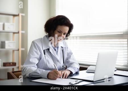 Lächelnde Ärztin mittleren Alters, die Notizen auf Papier schreibt. Stockfoto