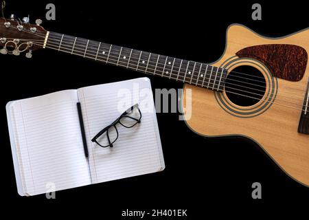 Klassische Akustikgitarre und ein offenes Notizbuch auf schwarzem Hintergrund. Stockfoto