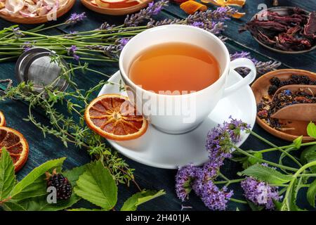 Tee. Kräuter, Blumen und Früchte rund um eine Tasse Tee, auf einem dunklen rustikalen Hintergrund Stockfoto
