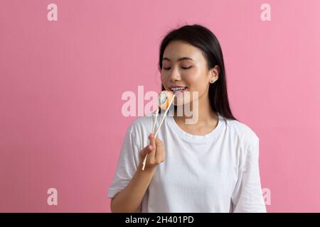 Asiatische Schönheit Modell Mädchen essen Sushi roll, gesunde japanische Lebensmittel. Schöne Frau, die Essstäbchen mit Philadelfia-Rolle hält Stockfoto