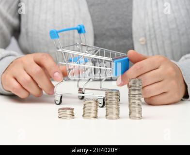 Die Frau sitzt am Tisch und hält einen Miniaturwagen und Stapel weißer Münzen. Konzept der Einsparungen Stockfoto