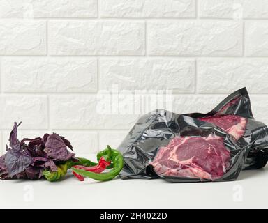 Rohes Rindfleisch, Chilischoten, ein paar Basilikum auf einem Tisch im Vakuum verpackt Stockfoto