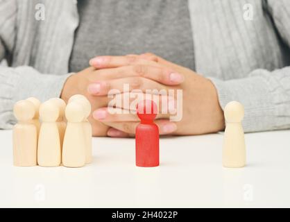 Gruppe von Holzfiguren, und eine stehend. Zwischen ihnen befindet sich eine rote Holzfigur des Verhandlungsführers. Einen Kompromiss finden, di Stockfoto