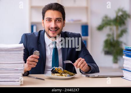 Junger Geschäftsmann, der einen Wecker isst Stockfoto