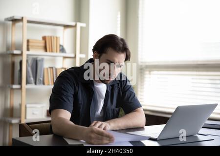 Gestresster junger Geschäftsmann, der das Papierdokument überprüft. Stockfoto