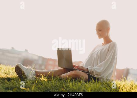 Millenial junge Frau blonde kurze Haare im Freien lächelnd Porträt mit Laptop. Stockfoto