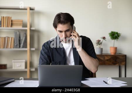 Fokussierter, qualifizierter junger Geschäftsmann, der im modernen Büro multitasking. Stockfoto