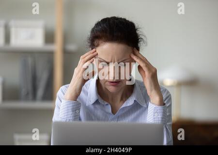 Ungesunde alte Geschäftsfrau, die unter Kopfschmerzen leidet. Stockfoto