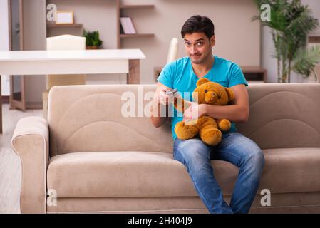 Junger Mann, der zu Hause mit Bärenspielzeug sitzt Stockfoto
