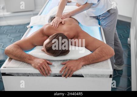 Der Mann liegt auf einer bequemen Couch, während ihm die Chiropraktikin im Krankenhaus eine Rückenmassage zuführt Stockfoto