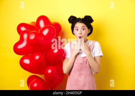 Valentinstag-Konzept. Beeindruckt koreanisches Mädchen sagen wow, keuchen und halten die Hände in der Nähe von geöffnetem Mund, starrte auf Kamera überrascht, Stockfoto