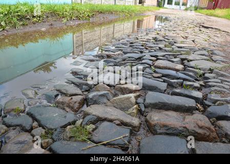 Alte graue gepflasterte Straße mit Pfützen in der alten europäischen Stadt. Stockfoto
