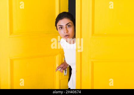 Junge inderin guckt durch die gelbe Tür. Stockfoto