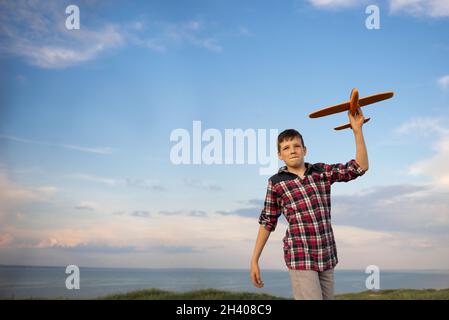Kind Pilot Flieger träumen zu reisen startet ein Spielzeug Flugzeug bei Sonnenuntergang. Junge auf einem Hintergrund von blauem Himmel fliegen ein Flugzeug. Ein aktiver Spaziergang in der Natur Stockfoto