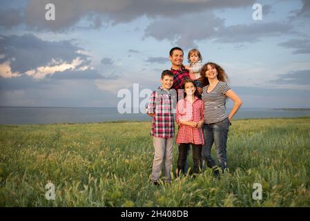 Fröhliche, freundliche große Familie mit drei Kindern zwei Söhne und eine Tochter stehen im Sommer bei Sonnenuntergang vor dem Hintergrund des wolkenblauen Himmels am Abend. Stockfoto