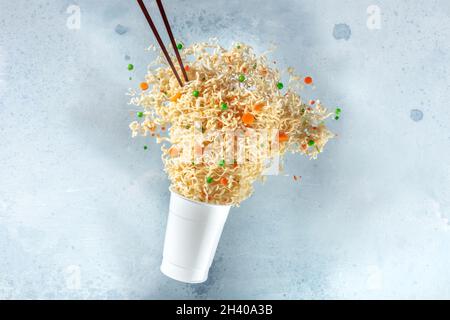 Ramen Tasse mit Instant-Nudeln fliegen aus ihm und Essstäbchen Stockfoto