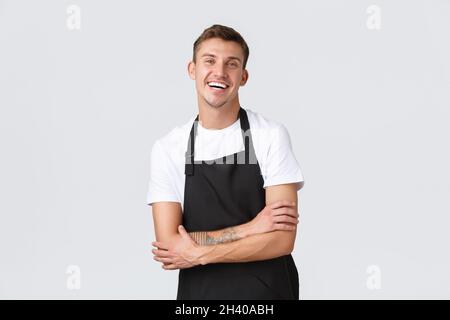 Inhaber von Kleinunternehmen, Café und Personalkonzept. Enthusiastisch lächelnd, gutaussehender Kellner in schwarzer Schürze, fröhlich lachend, se Stockfoto
