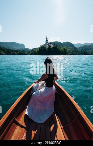 Ein Weibchen in einem weißen Rock, das auf einem Holzboot sitzt und zu einem Märchenschloss schwimmt Stockfoto