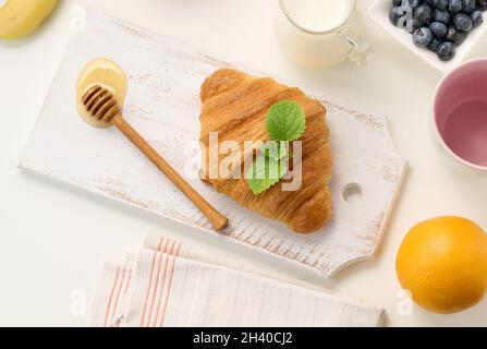 Frühstück am Morgen, frisch gebackene Croissants, Milch im Dekanter, Heidelbeeren und Honig Stockfoto