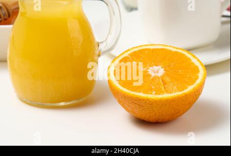 Eine halbe reife Orange und frisch gepresster Saft in einer transparenten Glasdekanter auf einem weißen Tisch Stockfoto