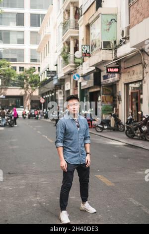 Porträt eines jungen, hübschen asiatischen Mannes im Denim-Hemd, der auf der Straße steht und mit Kopierraum auf die Kamera schaut. Chinesen Stockfoto